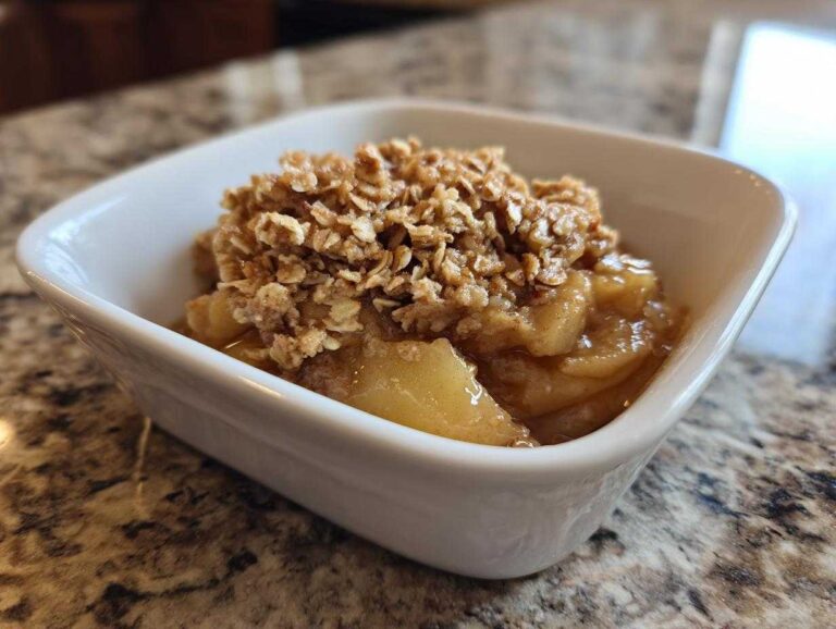 A single serving of healthy apple crisp in a white bowl, featuring a baked apple base and an oat topping.