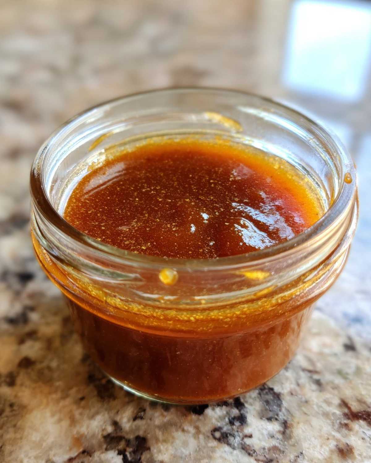 Close-up of homemade honey BBQ sauce in a glass jar, showcasing its rich color and texture.