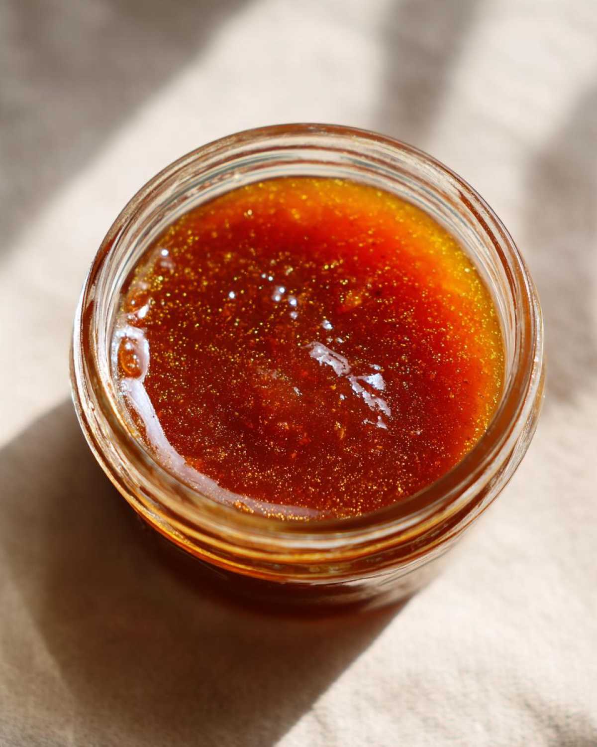 Overhead shot of homemade honey BBQ sauce in a clear glass jar, showing its rich color and texture.