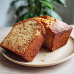 A loaf of honey vanilla banana bread with a slice cut, displayed on a plate.