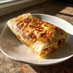 A delicious make ahead breakfast burrito on a white plate, showcasing its golden-brown tortilla and savory filling.