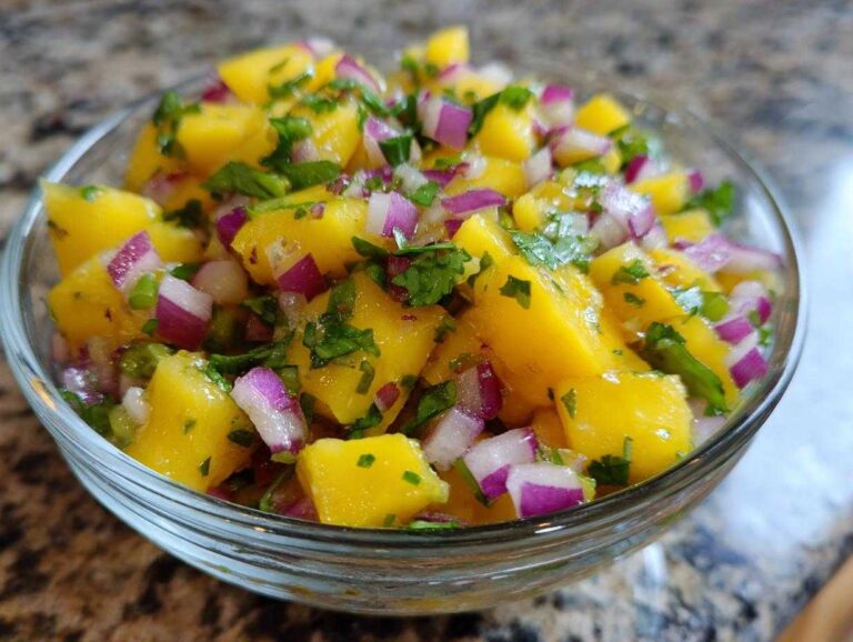 Close-up of vibrant mango salsa in a glass bowl, featuring diced mangoes, red onions, and cilantro.