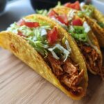 Close-up of crispy mini chicken tacos filled with shredded chicken, lettuce, and tomatoes.