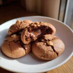 Delicious Nutella cookies on a white plate, one broken open to reveal a gooey Nutella center and hazelnut topping.