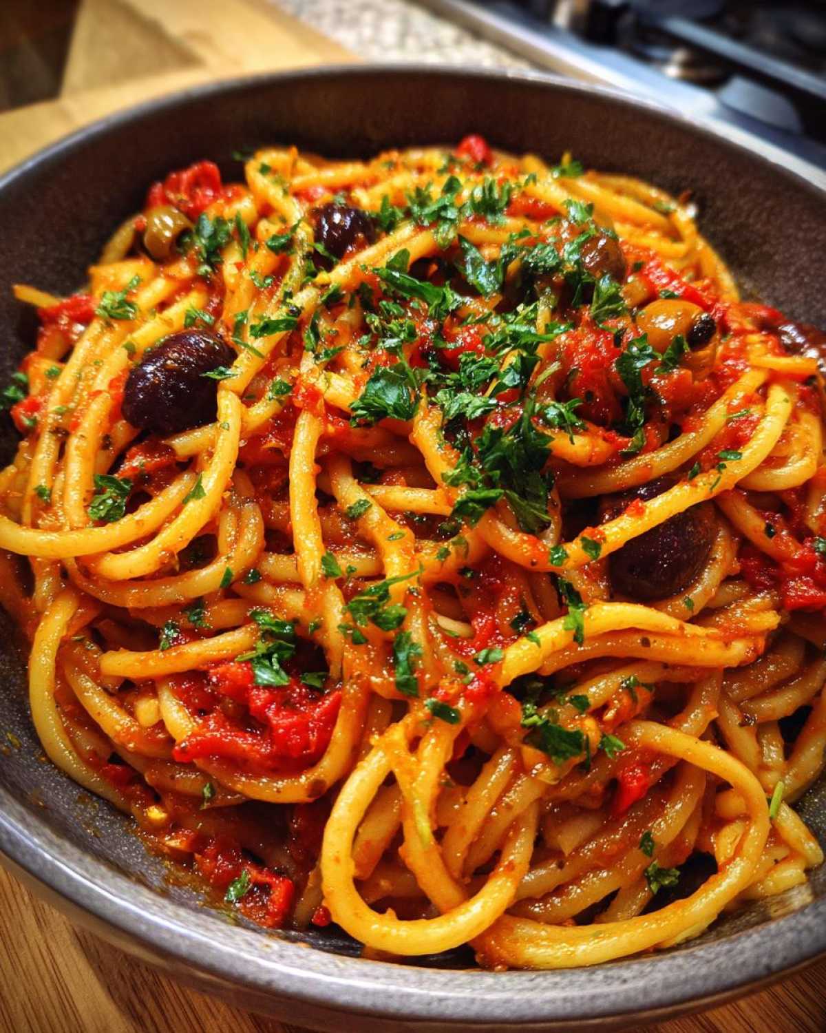 A bowl of one pan spicy pasta with tomato sauce, olives, and fresh parsley.