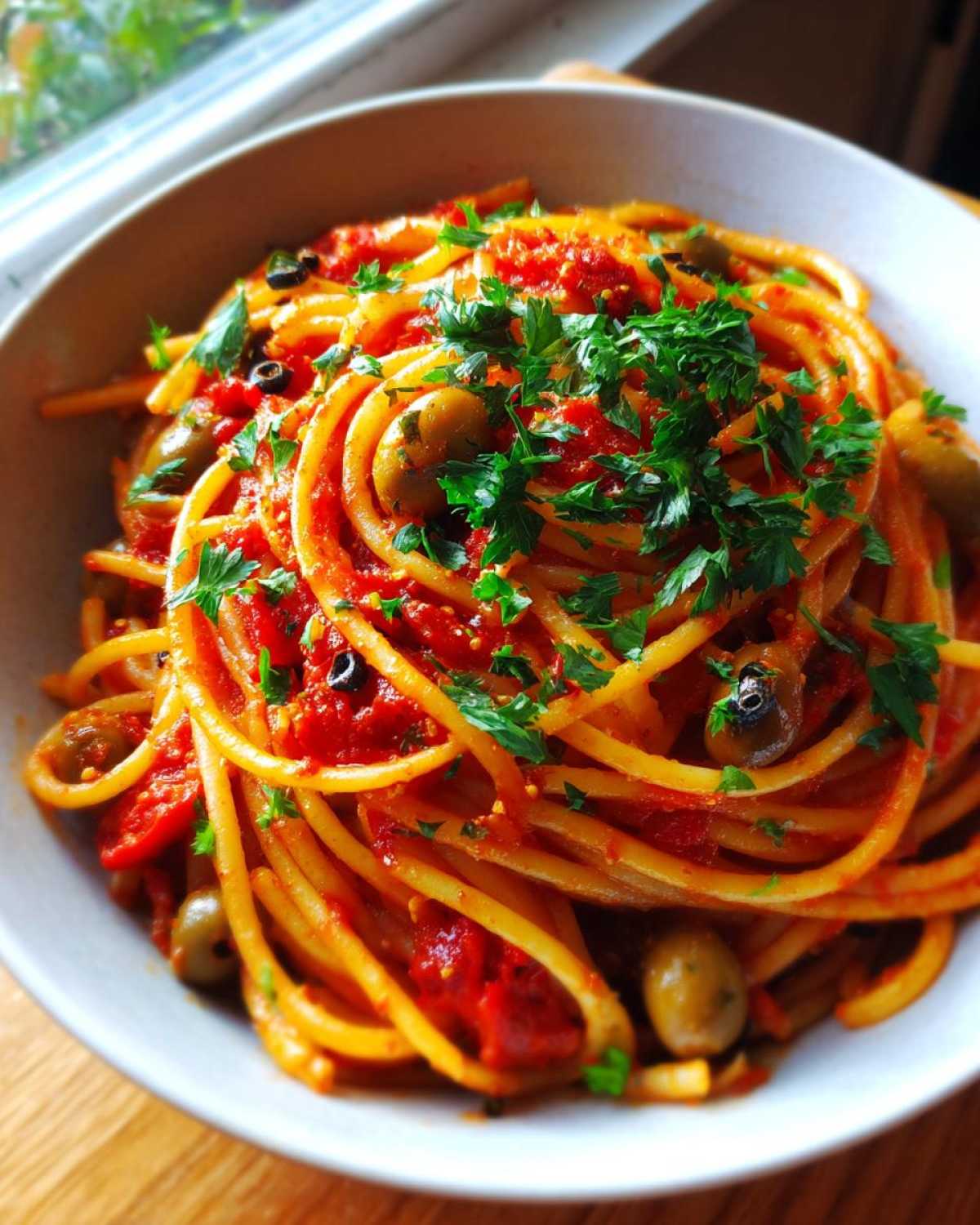 Close-up of one pan spicy pasta in a bowl, topped with tomato sauce, olives, and fresh parsley.