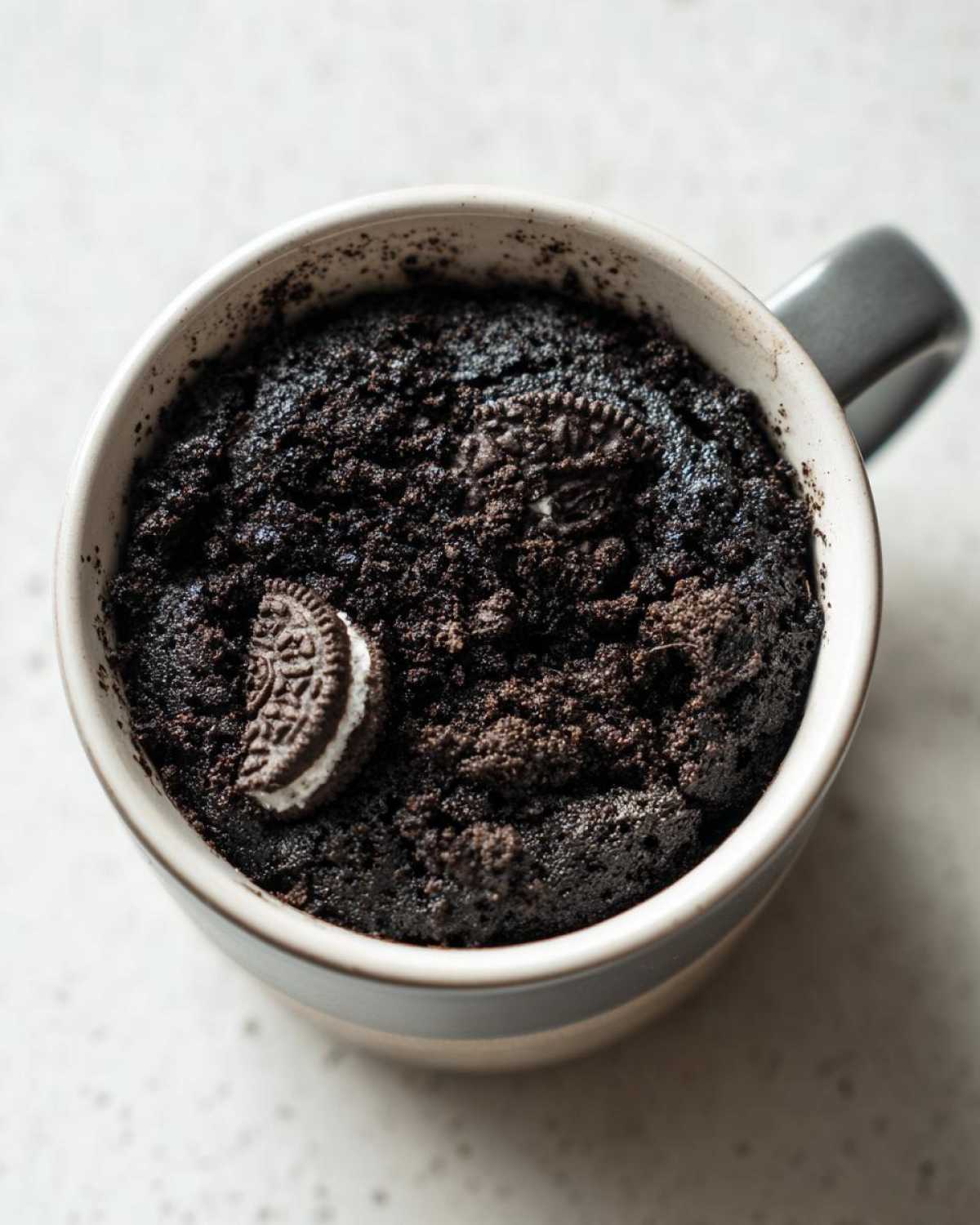 Top-down view of a freshly baked Oreo mug cake in a grey mug, topped with a halved Oreo cookie.