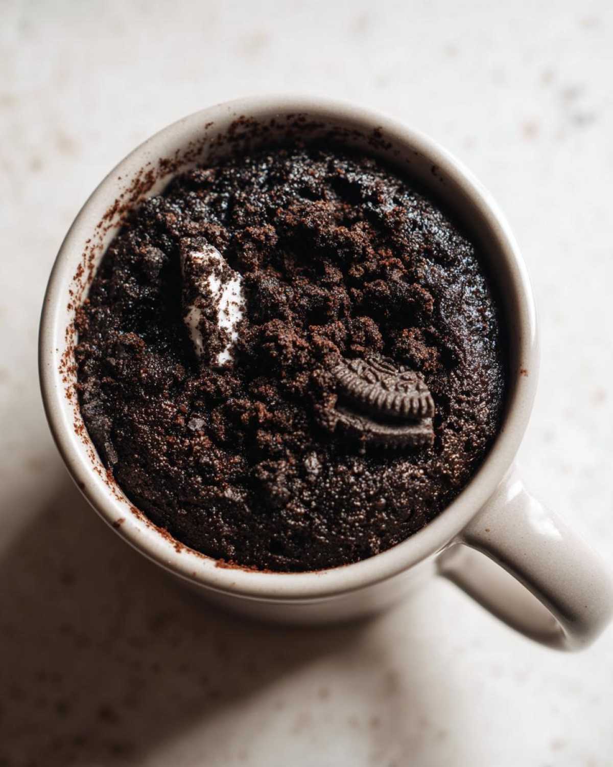 Overhead shot of a freshly baked Oreo mug cake in a mug, topped with an Oreo cookie piece.