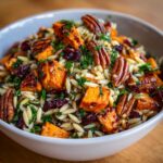 Close-up of orzo sweet potato salad with pecans, cranberries, and fresh herbs in a bowl.