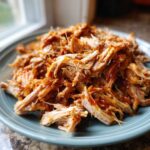 Close-up of Pioneer Woman slow cooker pulled pork, piled high on a blue plate with barbecue sauce.