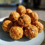 A stack of homemade pumpkin protein bites on a plate, topped with pumpkin seeds.