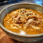A bowl of creamy slow cooker white chicken chili, topped with shredded chicken and fresh herbs.