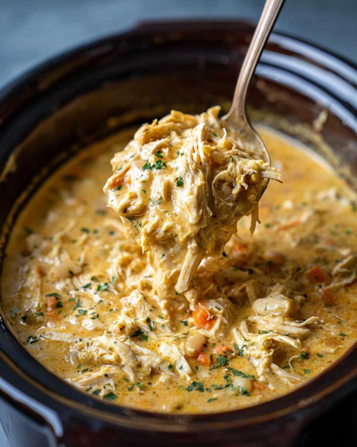 Spoonful of creamy slow cooker white chicken chili with shredded chicken, beans, and vegetables.