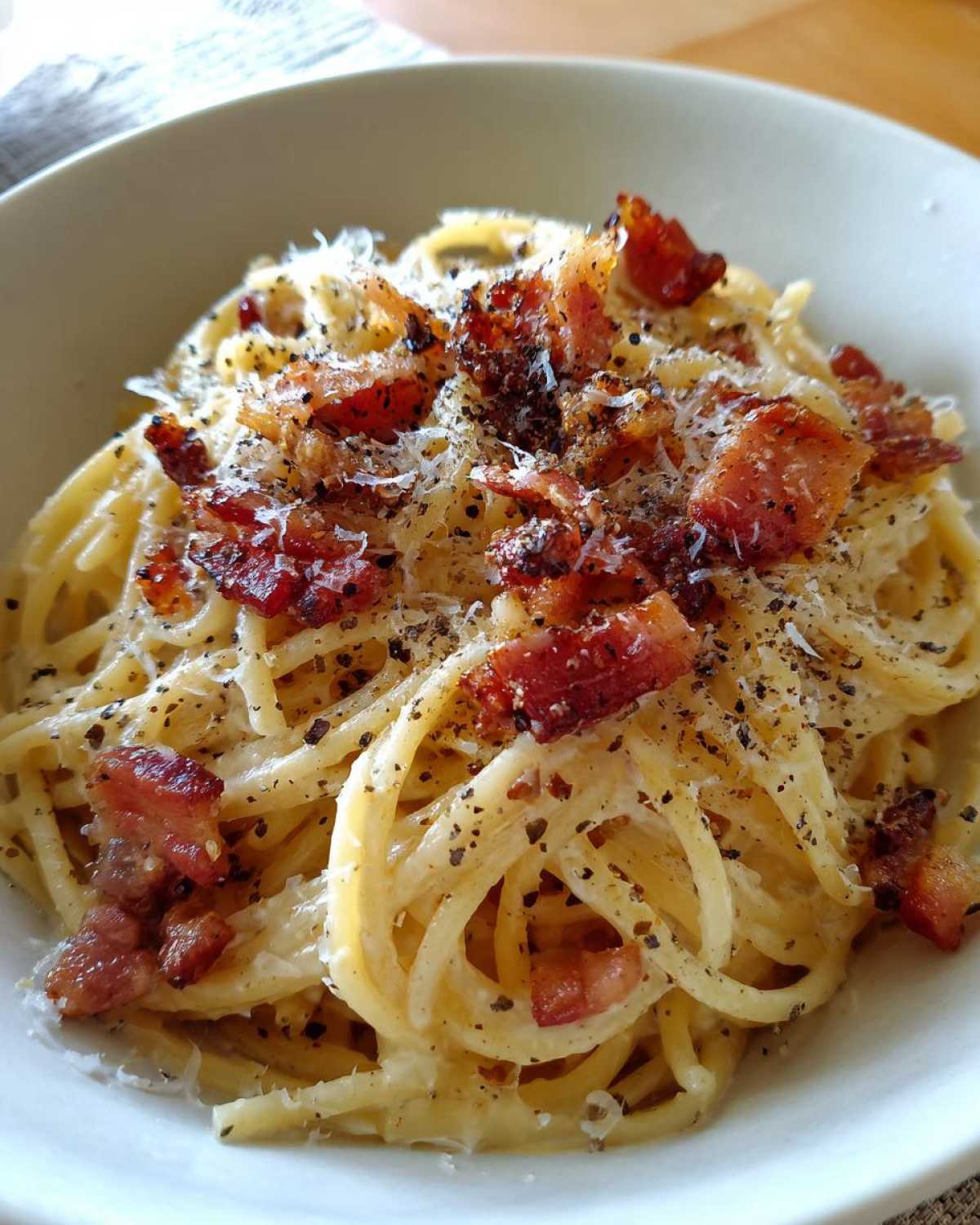 A bowl of creamy spaghetti carbonara topped with crispy bacon, parmesan cheese, and black pepper.