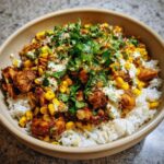 Overhead shot of a vibrant street corn chicken rice bowl, topped with cilantro and a creamy sauce.