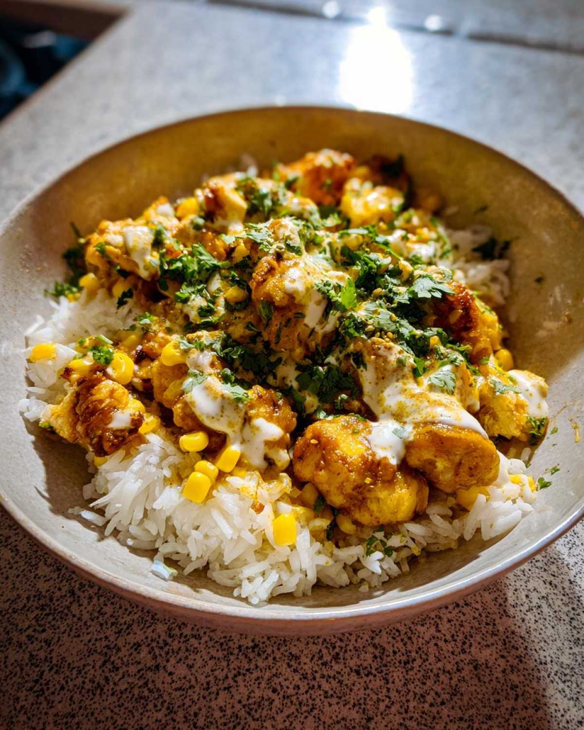 A flavorful street corn chicken rice bowl topped with cilantro and a creamy sauce.