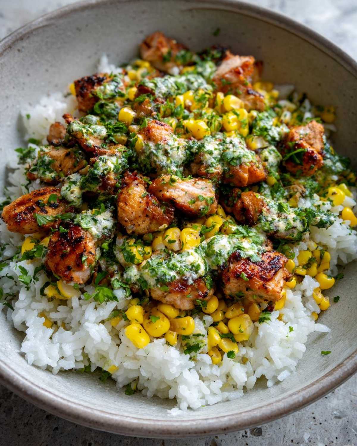 Close-up of a street corn chicken rice bowl with grilled chicken, corn, rice, and a creamy cilantro sauce.