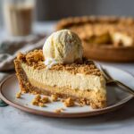 A slice of Amish peanut butter pie topped with a scoop of vanilla ice cream on a white plate.