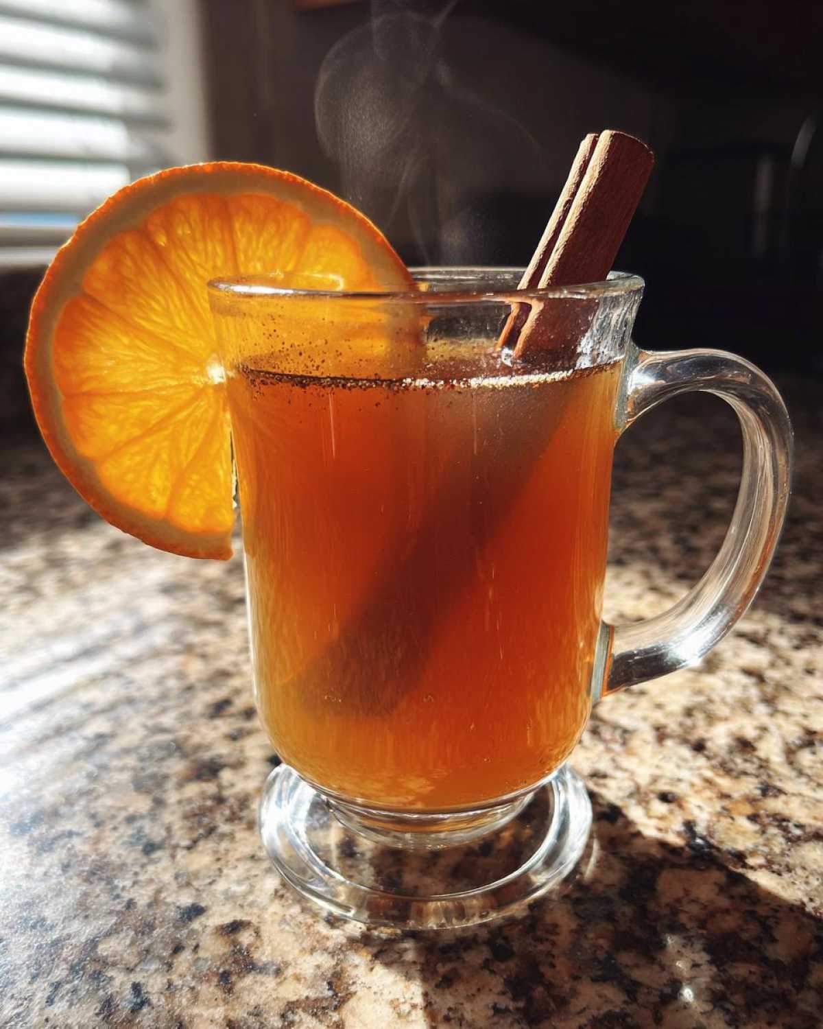 A steaming mug of apple cider garnished with an orange slice and cinnamon stick.