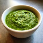 A bowl of vibrant green basil pesto, showcasing its fresh and creamy texture.