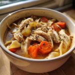 A comforting bowl of Chicken noodle soup with chicken, noodles, carrots, and herbs.