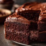 A slice of rich chocolate Gingerbread cake with chocolate frosting on a dark plate.