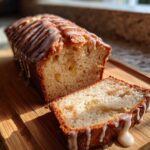 A loaf of cinnamon apple bread with icing, with a slice cut, sitting on a wooden board.