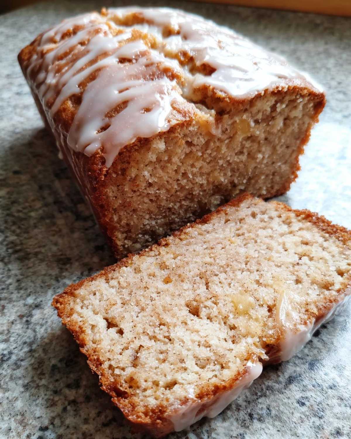 A loaf of cinnamon apple bread with icing, next to a freshly cut slice.