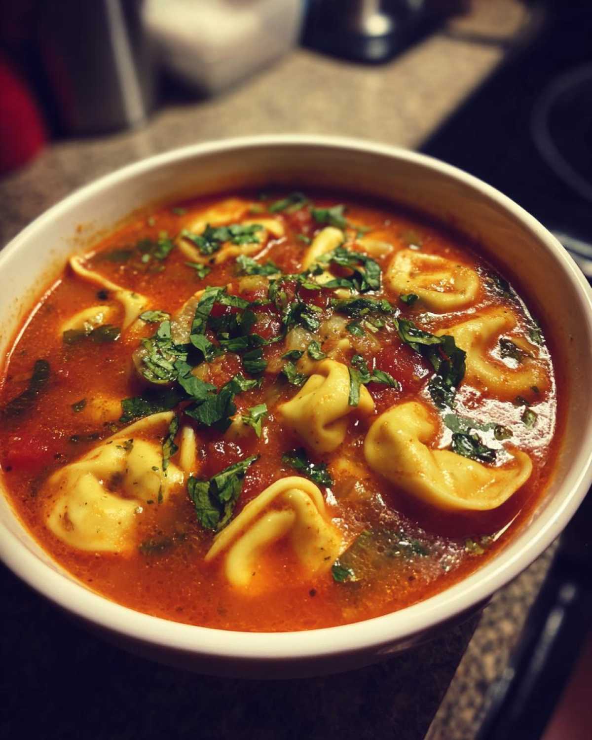A bowl of delicious crockpot tomato tortellini soup, garnished with fresh herbs and cheese.