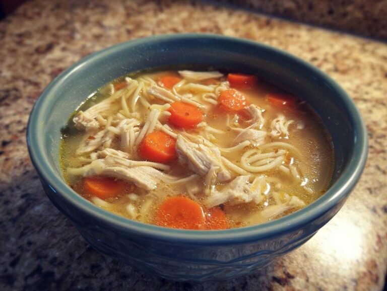 A bowl of Ginger garlic chicken noodle soup with carrots and shredded chicken.