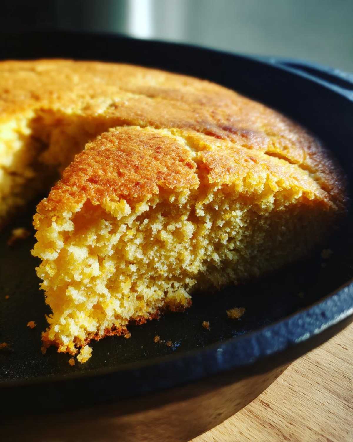 A slice of golden cornbread shown in a cast iron skillet, displaying its moist texture.