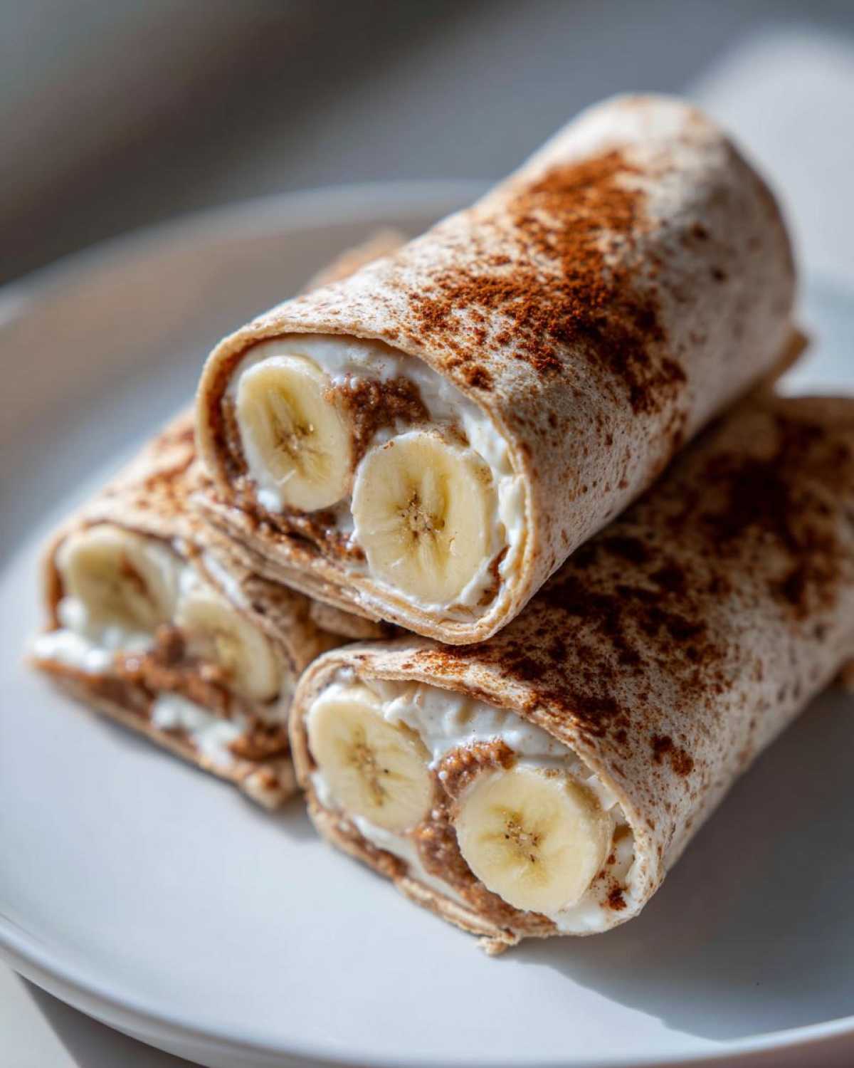 A stack of high protein banana roll-ups with visible banana slices, creamy filling, and cinnamon dusting.