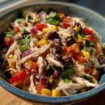 A vibrant bowl of Southwest chicken salad with shredded chicken, corn, black beans, red onion, and cilantro.