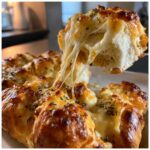A piece of cheesy Hawaiian roll garlic bread being pulled away, showing long, melted cheese strings.
