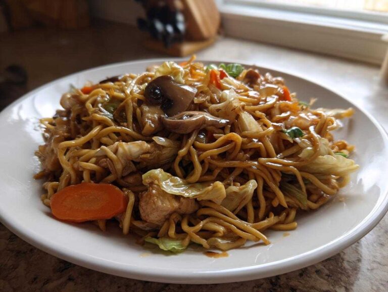 A close-up of a serving of savory chicken chow mein recipe featuring noodles, cabbage, carrots, and mushrooms.
