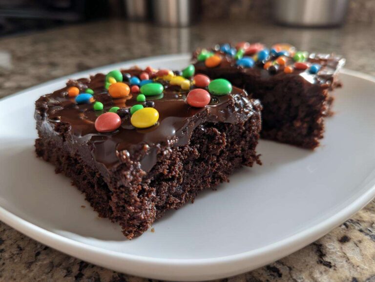 Two rich, fudgy slices of cosmic brownies topped with glossy chocolate frosting and colorful candy-coated chocolates.
