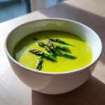 A bright green bowl of creamy asparagus soup topped with fresh, cooked asparagus tips.