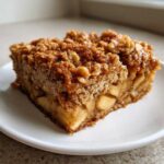 A square slice of apple baked oatmeal with a thick, caramelized crumble topping served on a white plate.