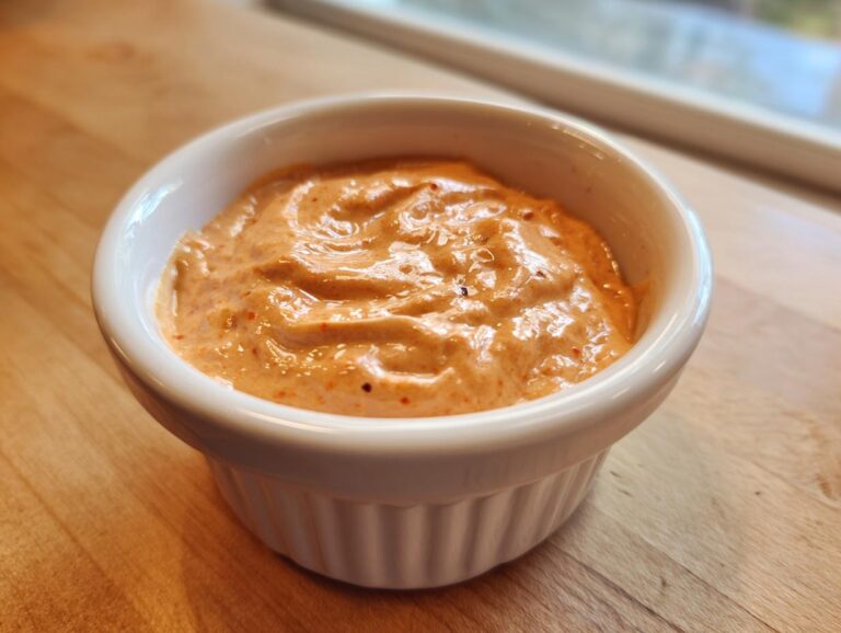 Close-up of creamy, orange-tinted big mac sauce served in a small white ramekin on a wooden surface.