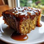 A close-up of a moist slice of sticky toffee pudding recipe covered in rich, dripping toffee sauce.
