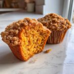 Close-up of a moist sweet potato muffin cut in half, showing the orange interior and brown streusel topping.