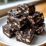 A tempting stack of rich, dark chocolate Oreo fudge squares filled with crushed cookies, served on a white plate.