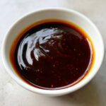 Close-up of thick, glossy homemade teriyaki sauce with visible spice flecks in a small white dipping bowl.