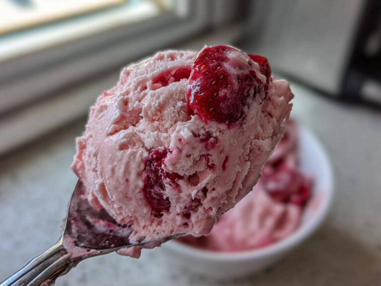 Close-up of a spoonful of pink strawberry ice cream topped with a piece of fresh strawberry.