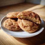 Close-up of soft snickerdoodle cookies, one broken in half to show the chewy interior, dusted with cinnamon sugar.