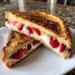 Two halves of golden brown stuffed french toast filled with cream cheese and fresh sliced strawberries.