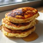 Close-up of a stack of three fluffy banana pancakes drizzled generously with golden syrup.