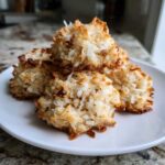 A small stack of golden brown, toasted coconut almond joy cookies on a white plate.