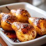 Four caramelized baked pears glistening with syrup and spices in a white baking dish.