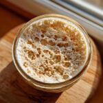 Top-down view of a very active sourdough starter in a glass jar, showing a thick layer of large, bubbly foam.